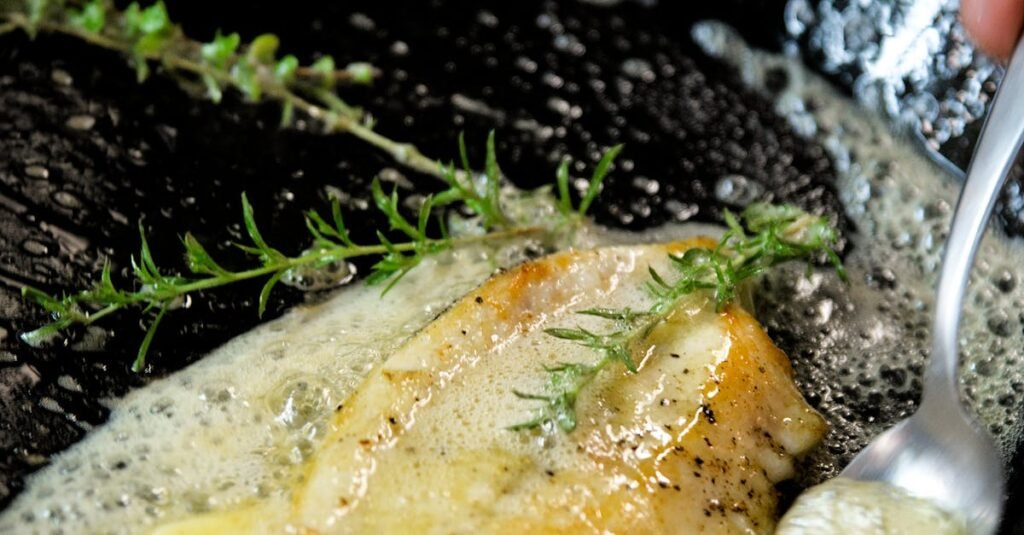Close-up of sole meunière frying with thyme and butter in a pan.