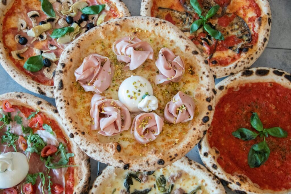 A top view of various Italian pizzas with fresh toppings like basil, mozzarella, and prosciutto.