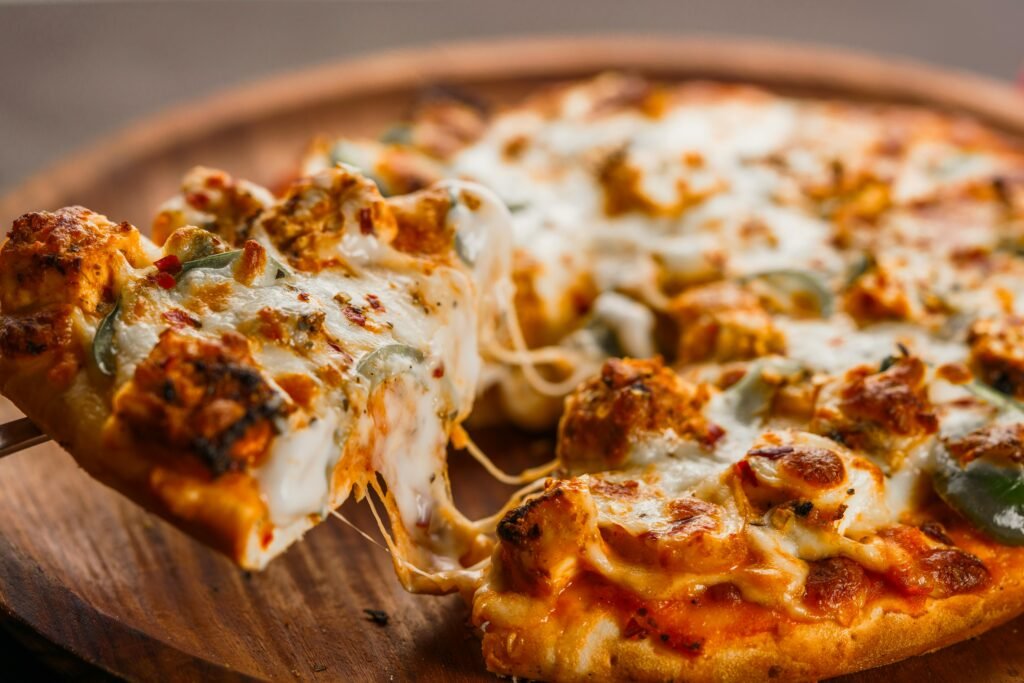 Close-up of a hot cheesy pizza being served with flavorful toppings on a wooden platter.