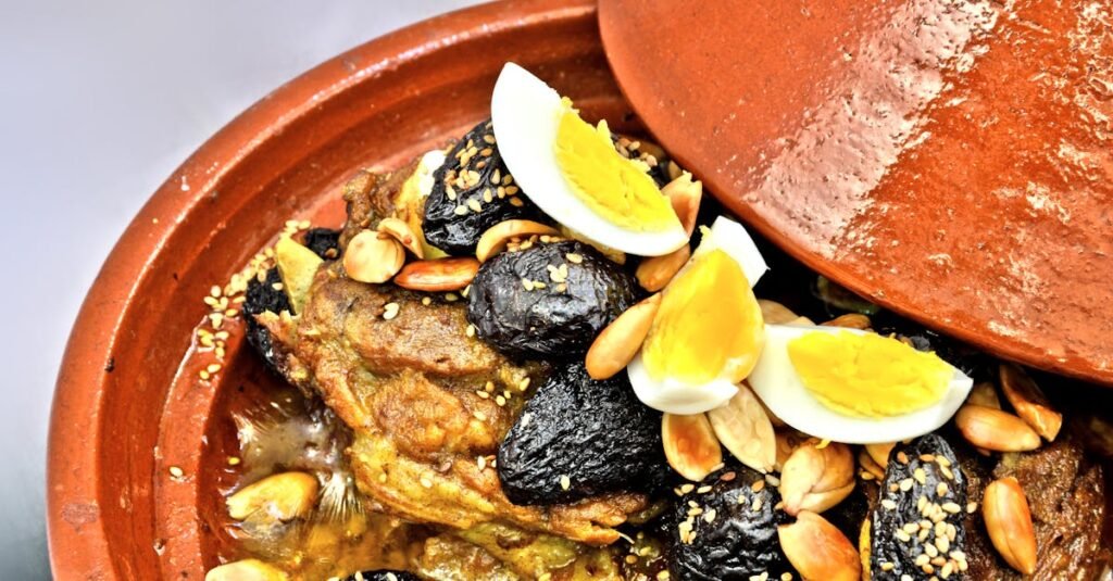Close-up of Moroccan lamb tagine with prunes, almonds, and boiled eggs in a clay pot.