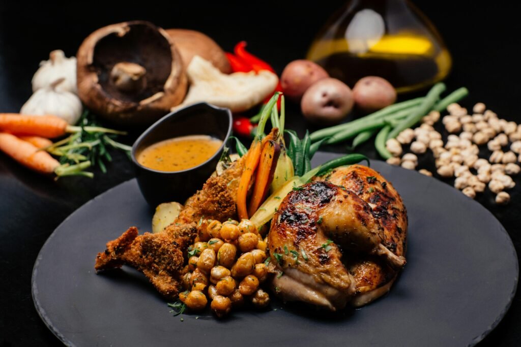 Deliciously spiced chicken with roasted vegetables and chickpeas on a black plate.