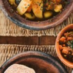 Delicious Moroccan dishes served with fresh vegetables and traditional bread on a woven mat.