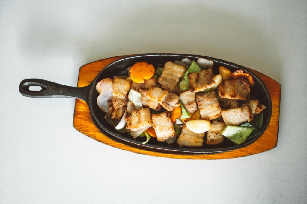 Tasty grilled pork belly served with vegetables on a cast-iron skillet, perfect for a delicious meal.