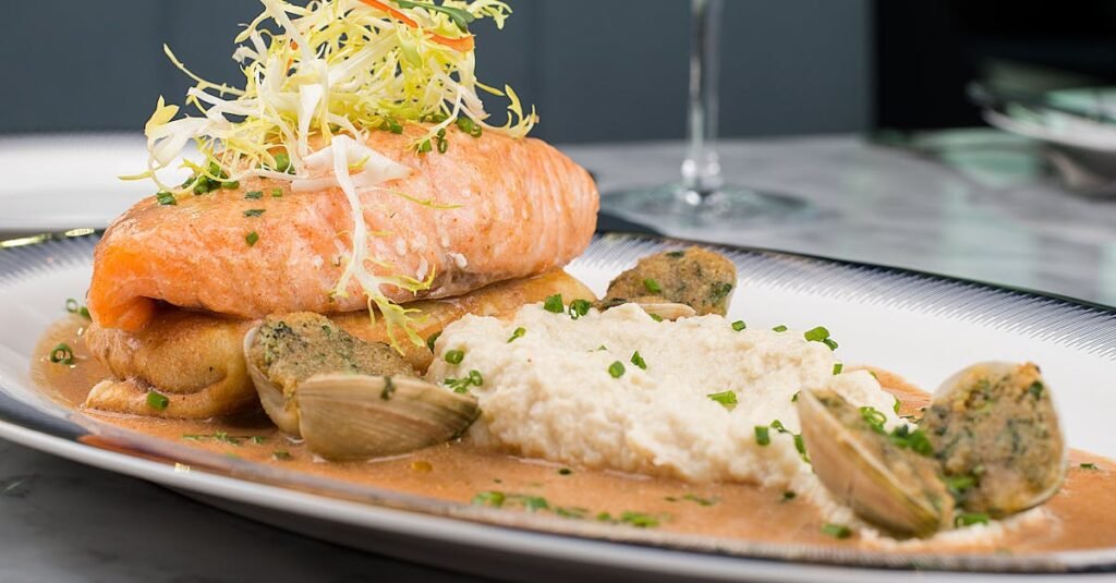 Delicious gourmet salmon dish with creamy mashed potatoes, clams, and fresh herb garnish.